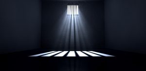An old jail cell interior with barred up window with light rays penetrating through it reflecting the image on the floor